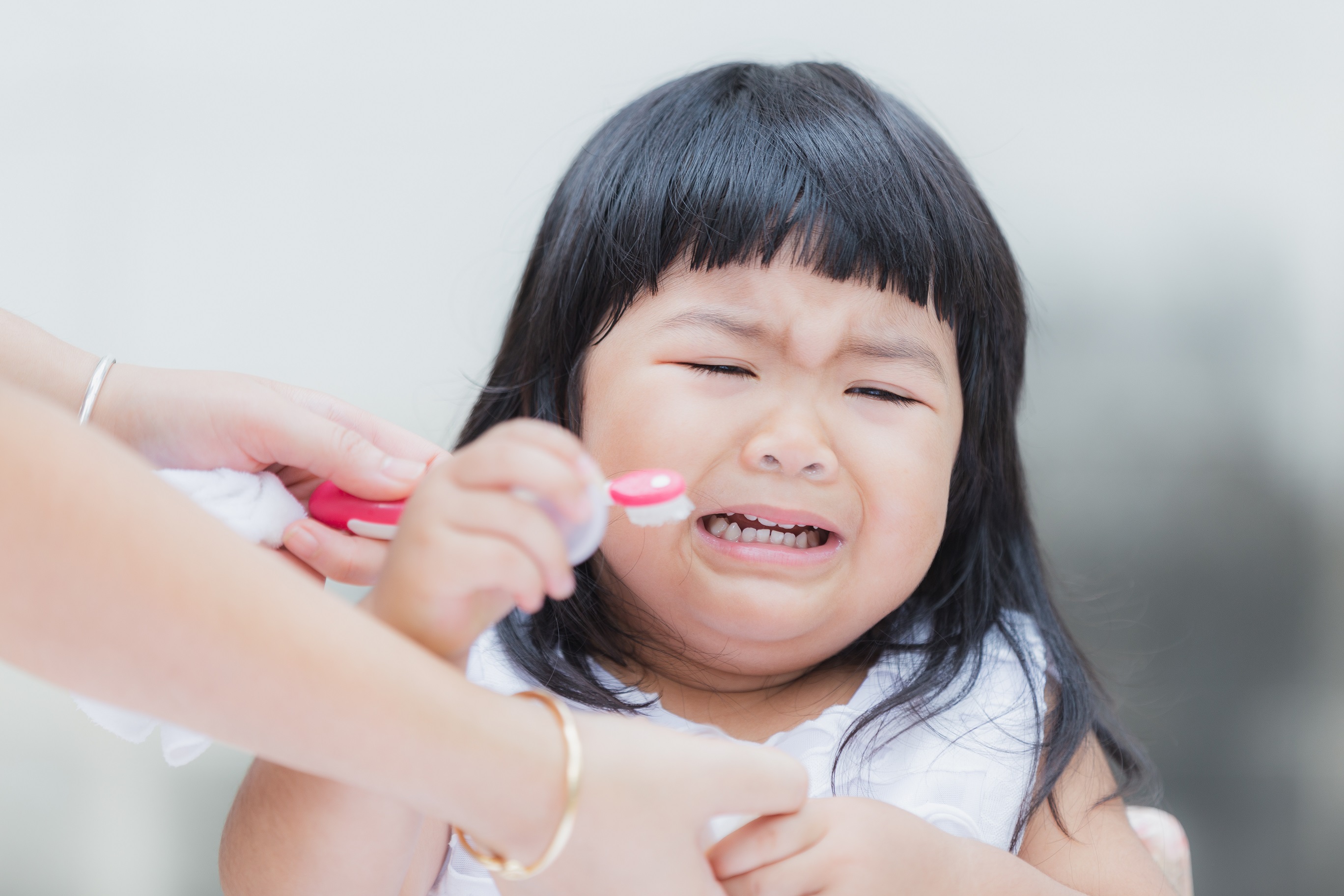 A struggling child refuses to brush her teeth